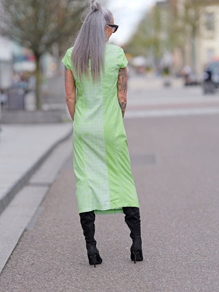 Frau im langen Rundholz Kleid, kombiniert mit schwarzen Stiefeln. Das Kleid zeigt eleganten Straßenmodestil und hebt sich durch seine beeindruckende Verarbeitung aus 70% Viskose hervor.
