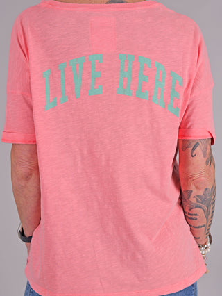 Person mit Tattoos trägt das One Tee Margareth coral, ein kurzärmeliges T-Shirt mit auffälligem Print vorne und hinten, aus 100% Baumwolle.
