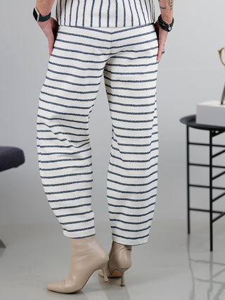 Person trägt die SOHO-t Pant Dune beige blue mit gestreiftem Design und geradem, leicht weitem Schnitt. Sichtbar sind Gummizug am Bund und Schuhe, die das Outfit ergänzen.