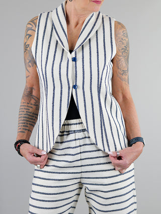 SOHO-t Gilet Gilda beige blue getragen von Person mit tätowiertem Arm, zeigt Knopfschlaufen vorne und ein modisches Streifenmuster. Aus 76% Baumwolle und 24% Polyester gefertigt.