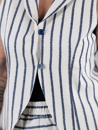 Eine Person trägt das SOHO-t Gilet Gilda beige blue mit Knopfschlaufe vorne, kombiniert mit einem gestreiften Hemd und gestreifter Hose, aus 76% Baumwolle und 24% Polyester.