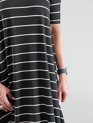 SOHO-t Kleid Anna schwarz/weiß: Nahaufnahme eines gestreiften Kleides mit asymmetrischem Schnitt, getragen von einer Person. Sichtbar sind ein Gürtel und eine Armbanduhr am Handgelenk.