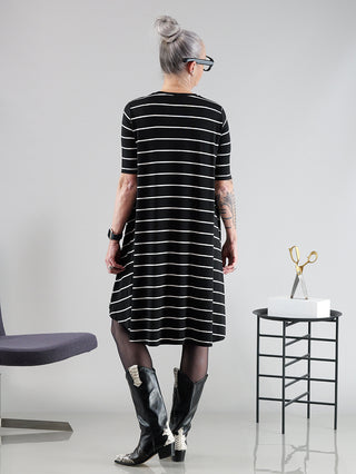 Frau trägt das SOHO-t Anna Kleid in Schwarz/Weiß mit asymmetrischem Schnitt, aus 94% Viskose und 6% Elastan. Kleid fällt größer aus, Modell ist 172 cm groß und trägt Größe XS.
