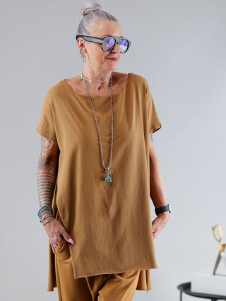 Frau trägt SOHO-t T-Shirt Mogano zimt mit rundem Ausschnitt, lässigem Schnitt und seitlichem Schlitz. Hinten länger geschnitten, kombiniert mit Sonnenbrille und Kette.