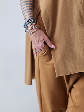 SOHO-t T-Shirt Mogano zimt, gezeigt mit einer Hand mit Armbändern, die in eine Jackentasche greift, lässige Tunika mit seitlichem Schlitz, hinten länger geschnitten, Rundhals.